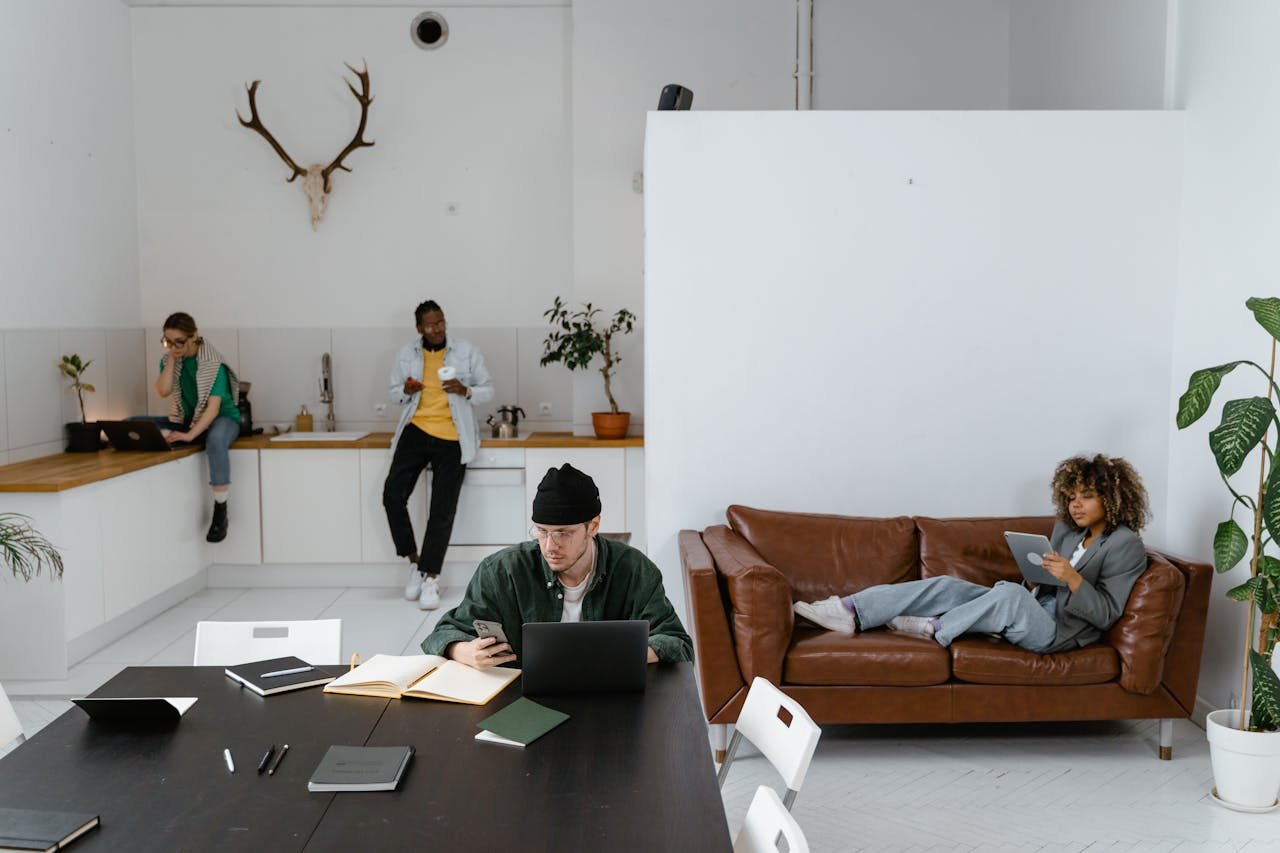 Diverse group of adults in a modern office using gadgets like laptops and tablets for work.